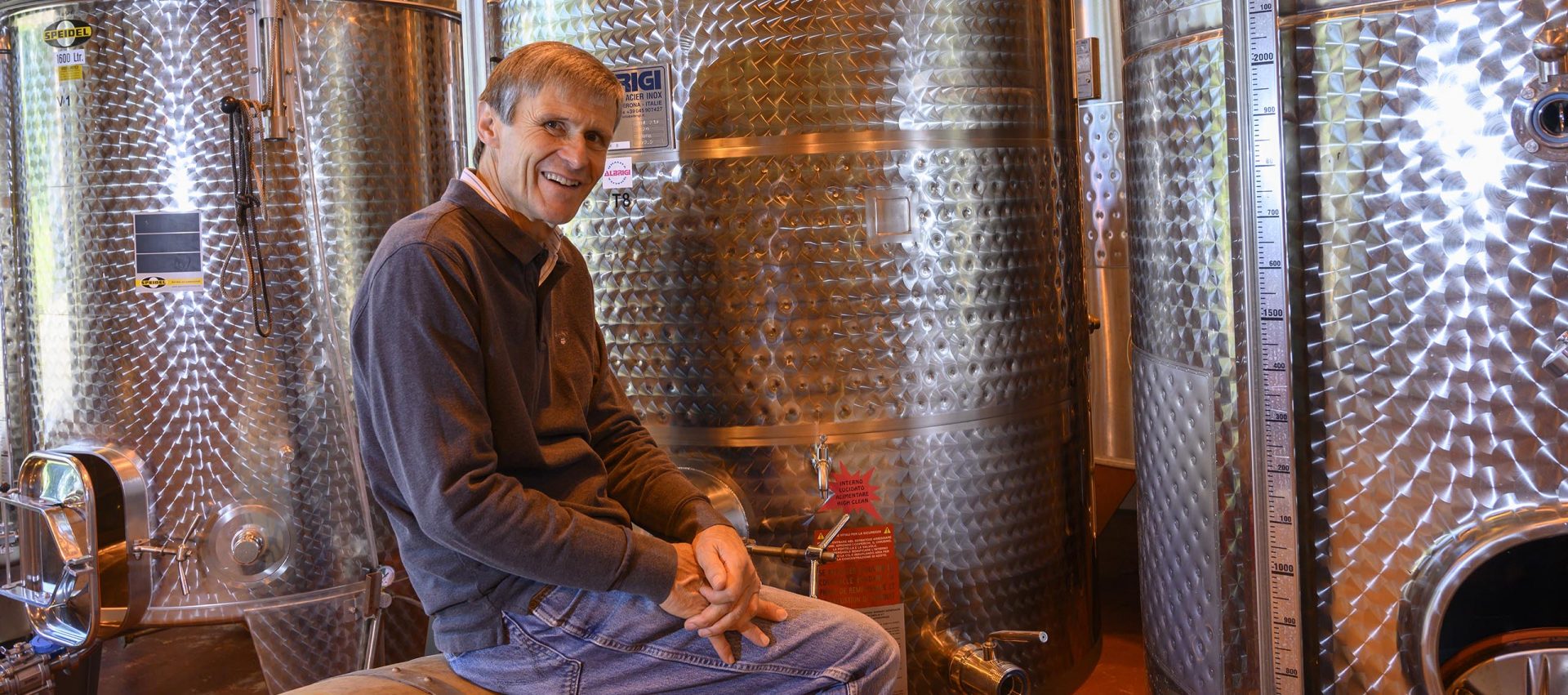 Picture of Ian Edwards, Winemaker and Owner, sitting infront of 3 stainless holding tanks.