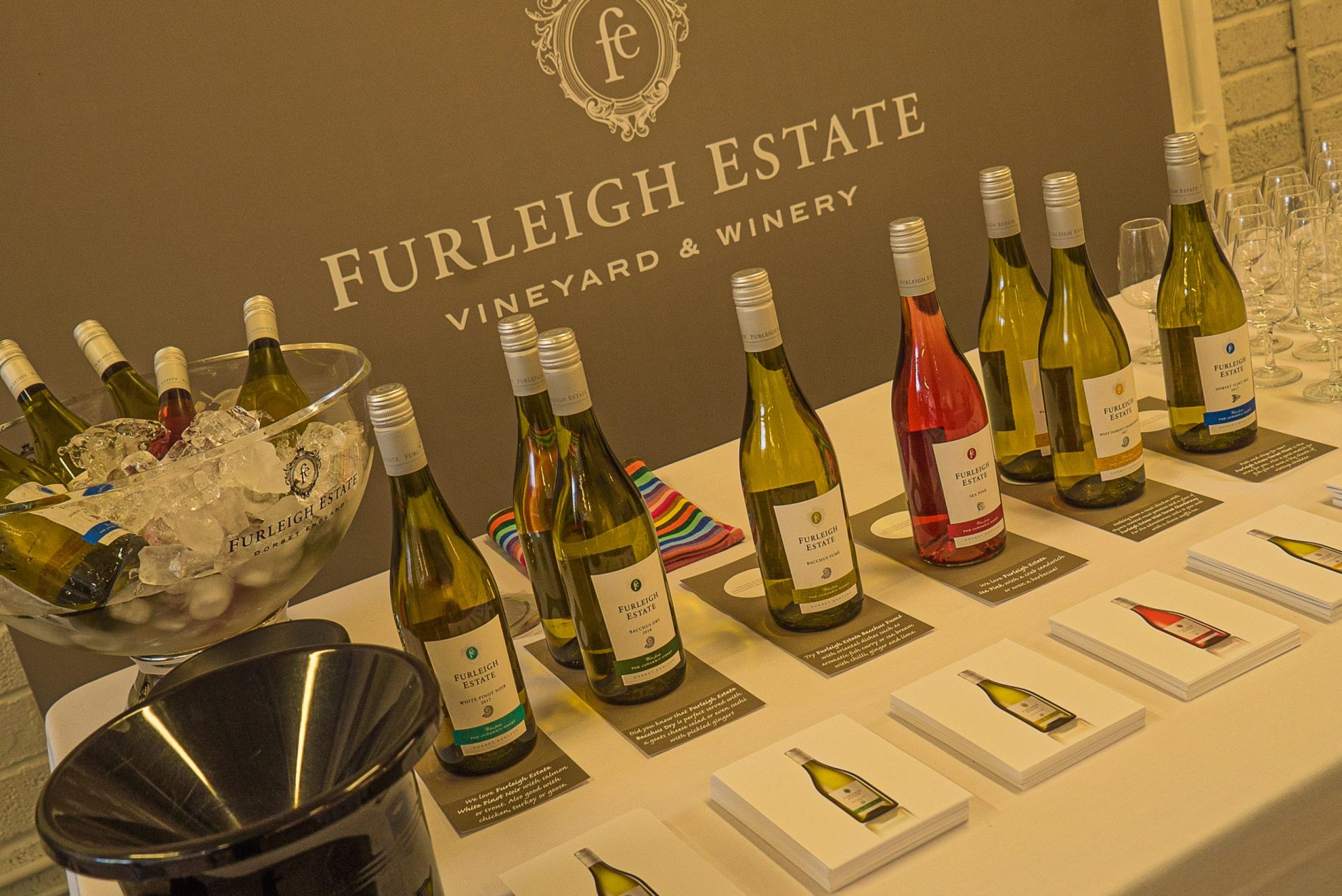A wine tasting table set up with various bottles of Furleigh Estate wines, informational pamphlets about the wines, and other assorted tasting supplies.