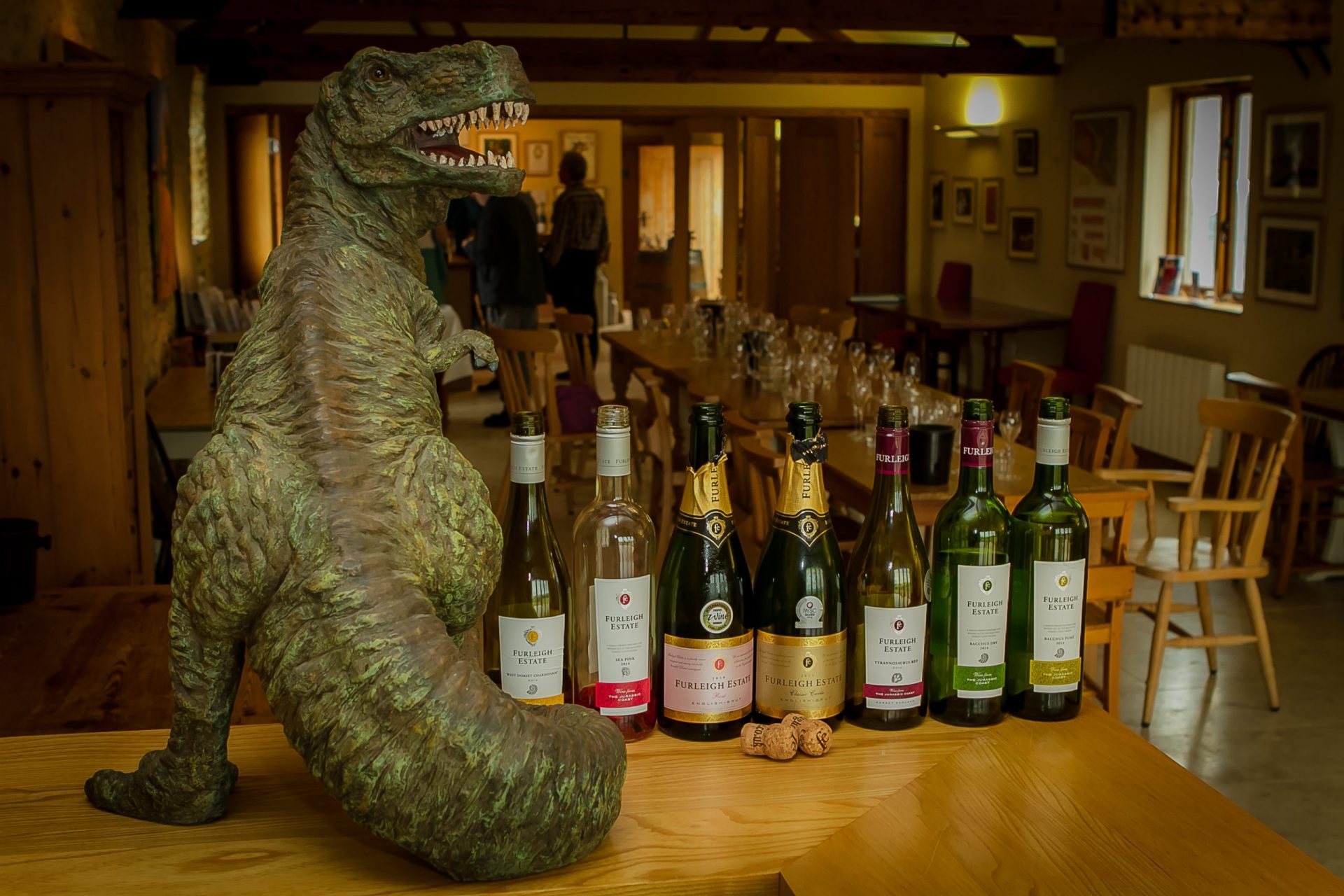 Picture of 7 assorted Furleigh Estate bottles on a wooden table with a dinosaur figurine beside them. 